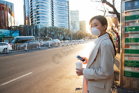 车站戴口罩公共交通戴口罩的年轻女人站在公交车站背景