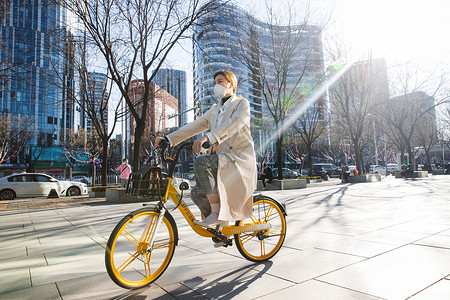 街道戴口罩的年轻女人骑共享单车高清图片