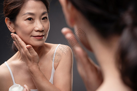 镜子反射对着镜子涂抹护肤品的中年女人背景