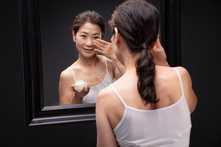 对着镜子涂抹护肤品的优雅女人图片