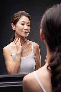 优雅的中年女人对着镜子做颈部护理图片