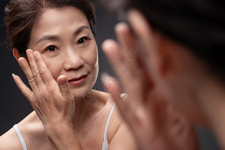 女性面部特写对着镜子做面部护理的中老年女背景