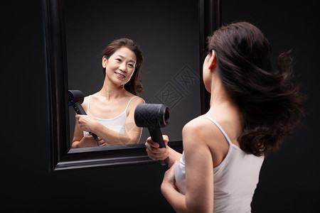 城市生活中年女人对着镜子用吹风机吹头发图片