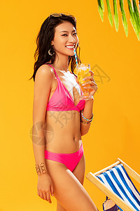 黄色背景感健康的沙滩上喝饮料的比基尼美女图片