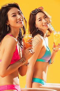东方人凉爽黄色背景快乐闺蜜在沙滩上喝饮料图片