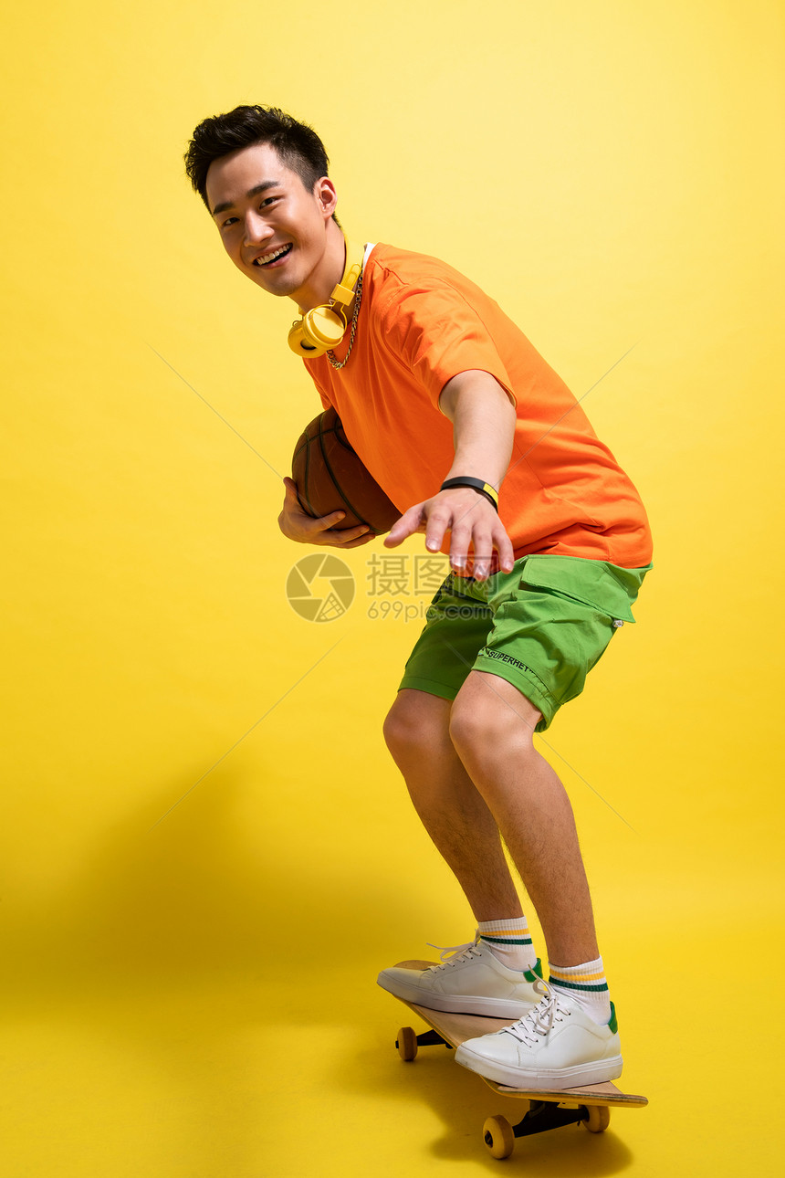 抱着篮球滑着滑板的青年男人图片