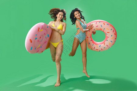 两个甜甜圈穿比基尼的肤色差闺蜜拿着游泳圈背景