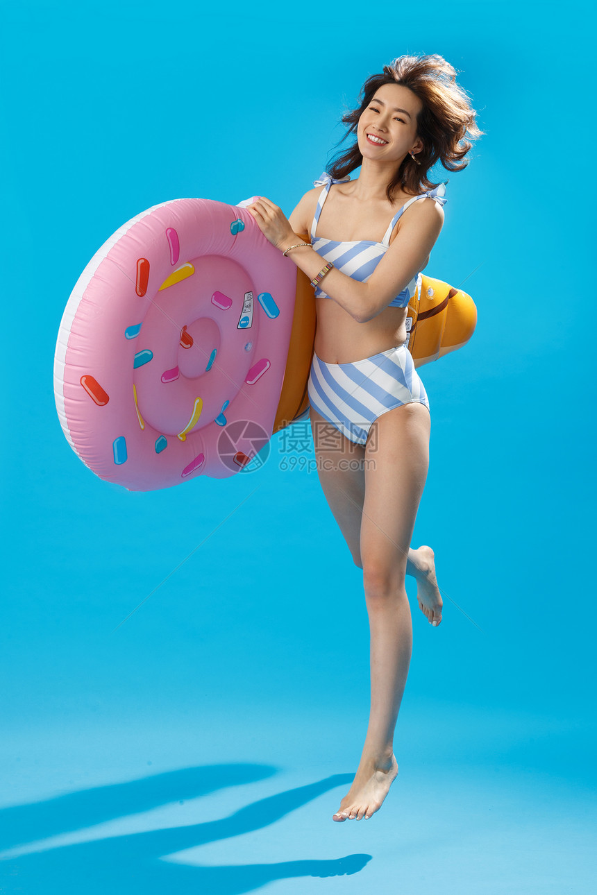 活力20多岁泳装抱着冰淇淋形状的浮排跳跃的比基尼美女图片