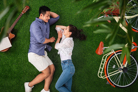 人青年伴侣面对面躺在草地上图片