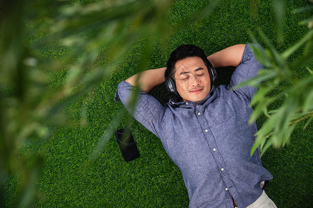 躺在草地上听音乐的青年男人图片