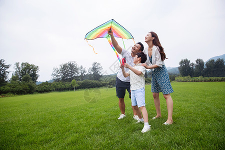 亲情山双亲家庭快乐的一家三口在草地上放风筝高清图片