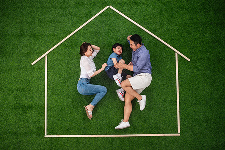 绿色表情箭头正上方视角25岁到29岁陪伴快乐的一家三口躺在草地上的房子轮廓里玩耍背景