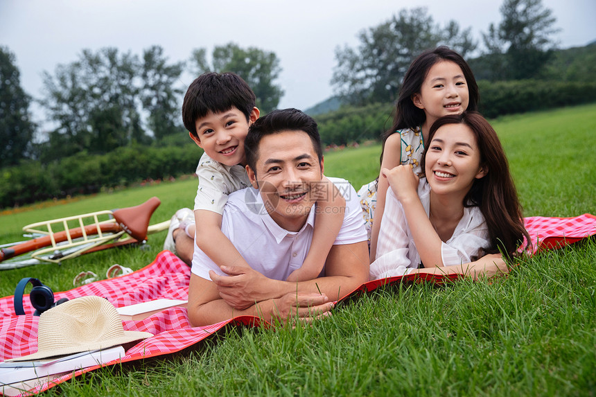 亚洲双亲家庭女儿趴在野餐垫上幸福的一家四口图片