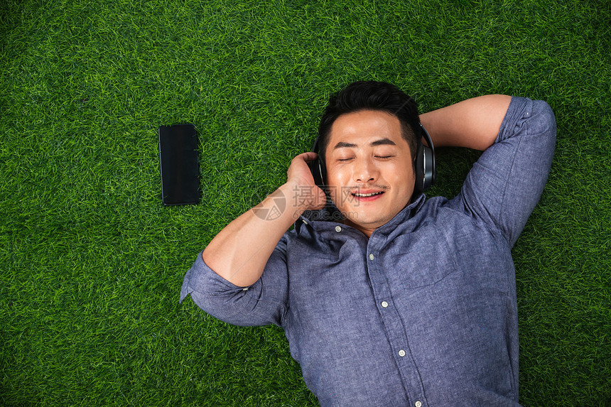 东方人东亚享乐躺在草地上听音乐的青年男人图片