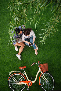 青年女人自然用手指指青年伴侣坐在草地上使用平板电脑高清图片