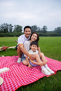 儿童布书乐趣成年人夏天幸福的一家三口坐在野餐垫上背景