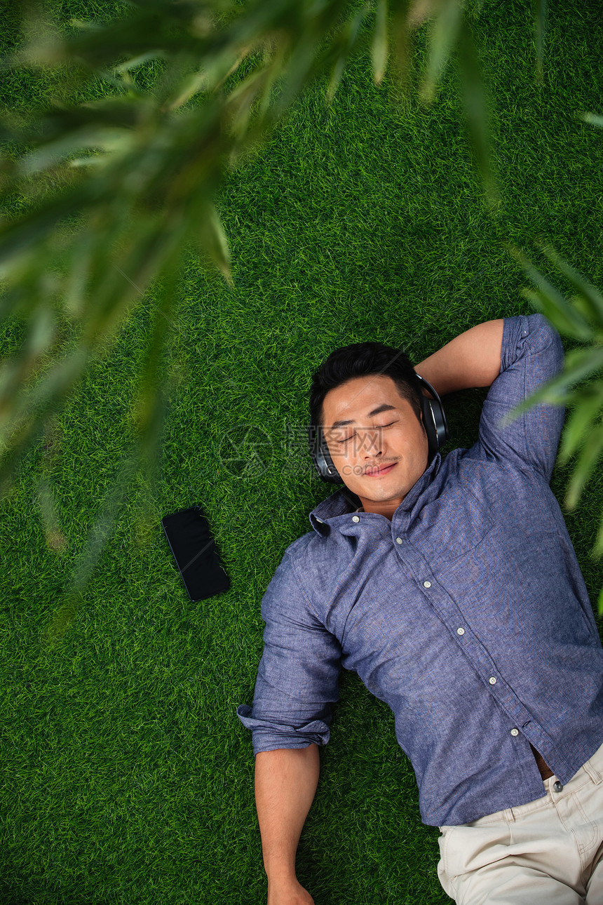 彩色图片不看镜头仰卧躺在草地上听音乐的青年男人图片
