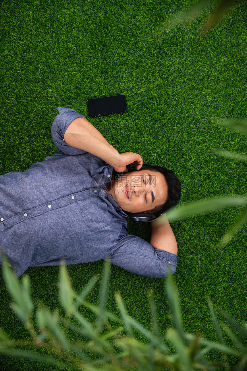 白昼微笑亚洲躺在草地上听音乐的青年男人图片