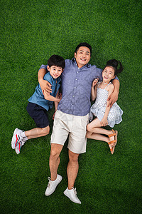 父亲搂着儿子和女儿躺在草地上图片