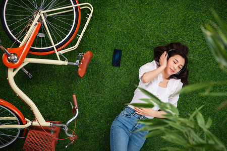 享受逃避现实假日躺在草地上听音乐的年轻女人图片