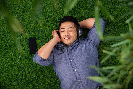 快乐的青年男人躺在草地上听音乐图片