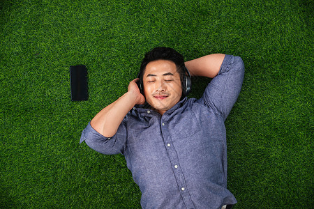 草坪自然度假青年男人躺在草地上听音乐图片