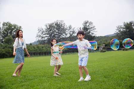 吹泡泡的母女东亚家庭相伴妈妈带着两个孩子在草地上快乐玩耍背景