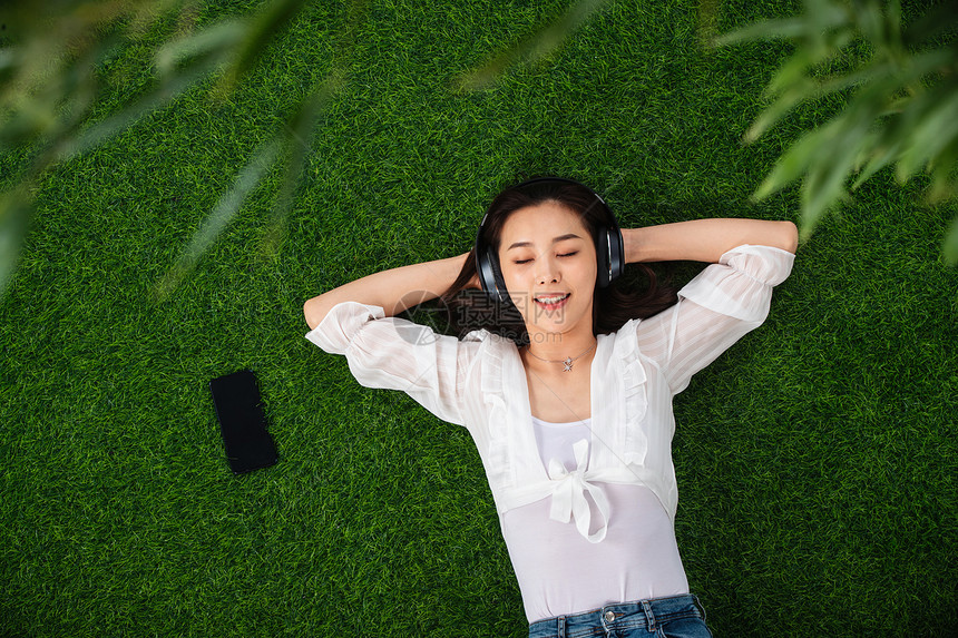 无忧无虑躺在草地上听音乐的青年女人图片