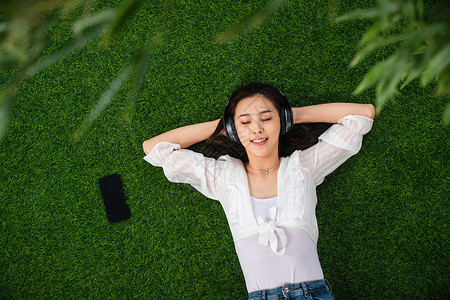 躺着听音乐无忧无虑躺在草地上听音乐的青年女人背景