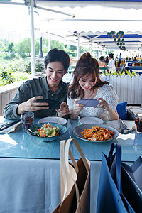 青年情侣在餐厅里用手机拍照高清图片