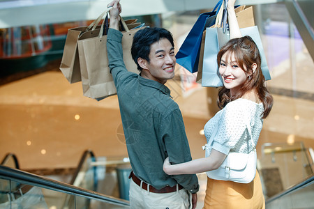 相伴购物搂着肩膀在商场里乘电梯的幸福情侣图片