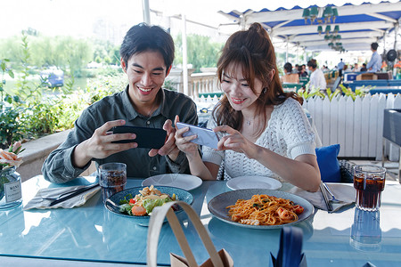 青年情侣在餐厅里用手机拍照背景图片