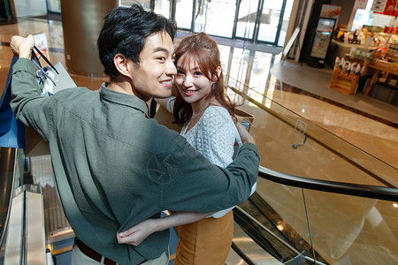 休闲装购物中心周末活动在商场里乘电梯的幸福情侣图片