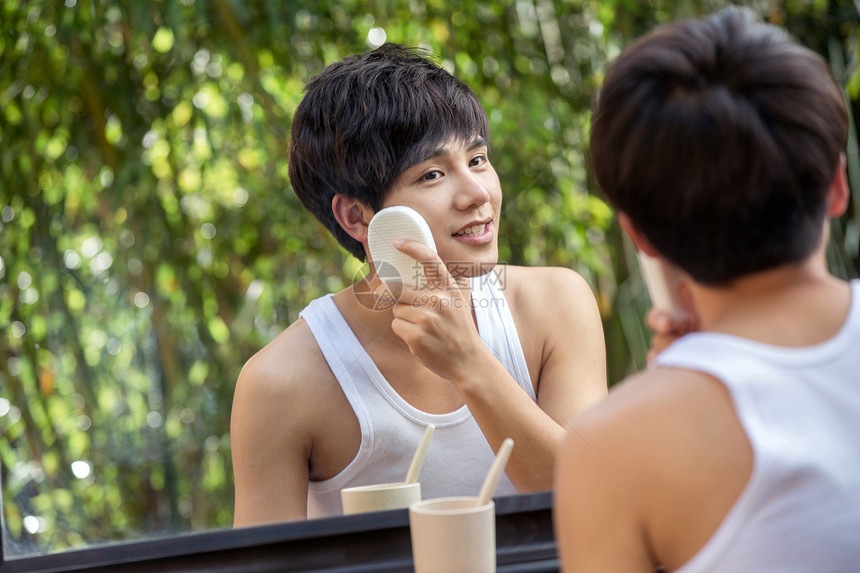 欣赏站着拿着户外对着镜子用面扑洗脸的年轻男人图片