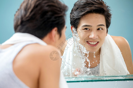 蓝色背景快乐背心年轻男人对着镜子洗脸图片