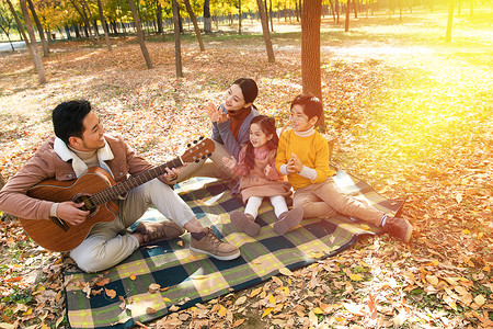爸爸坐着教女儿弹吉他幸福家庭在户外玩耍背景