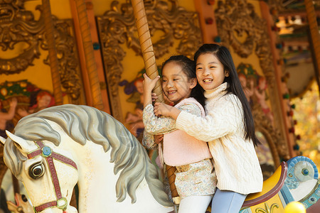 游乐园设施可爱的高兴的两个小女孩在玩旋转木马图片