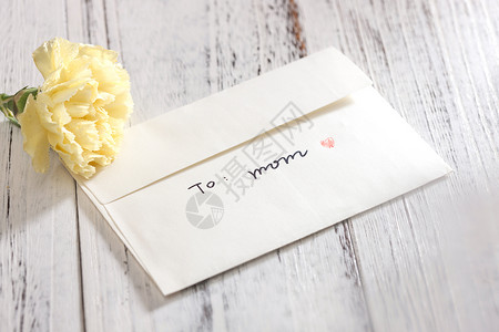 黄色福猪年贺卡桌上的康乃馨花和信封贺卡背景