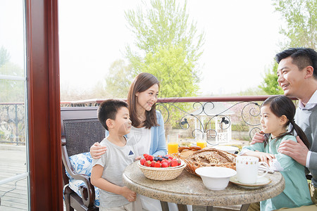 男孩坐在阳台上幸福家庭在阳台吃早餐背景