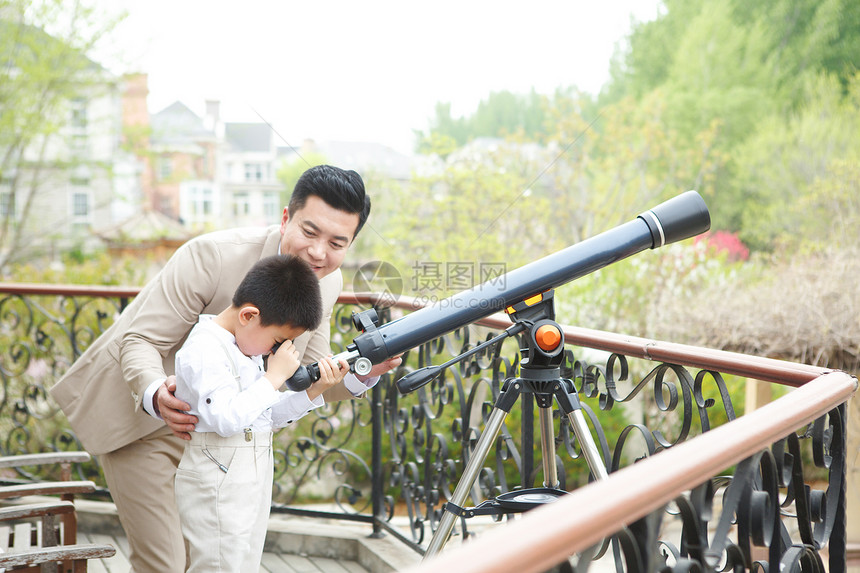 父亲和儿子在阳台使用天文望远镜图片