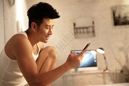 背心东方人清新青年男人在卧室玩手机图片