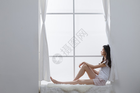 愉悦侧面视角家居服青年女人坐在窗户旁边高清图片