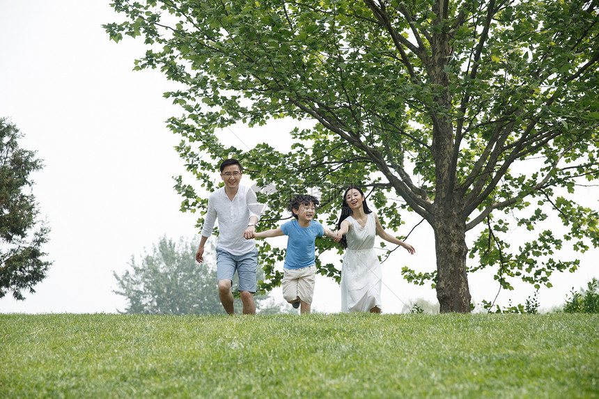白昼公园家庭一家三口在草地上奔跑图片