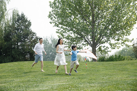 全身像愉悦家庭一家三口在草地上奔跑图片