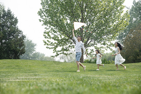 东方人人健康生活方式一家三口在草地上放风筝背景图片