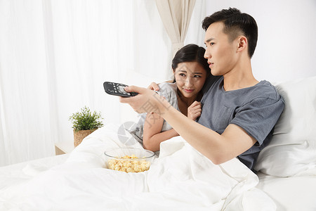 男人愉悦亚洲青年情侣坐着床上看电视图片