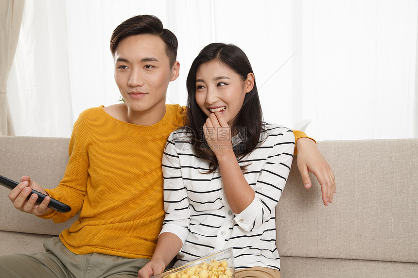 遥控器夫妇25岁到29岁青年情侣坐着沙发上看电视图片