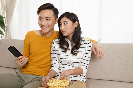 遥控器健康的20多岁青年情侣坐着沙发上看电视图片