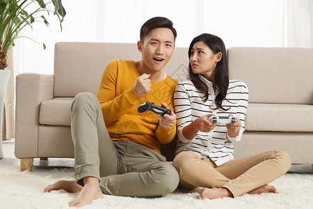 放松遥控器休闲装青年情侣坐着沙发上玩游戏图片