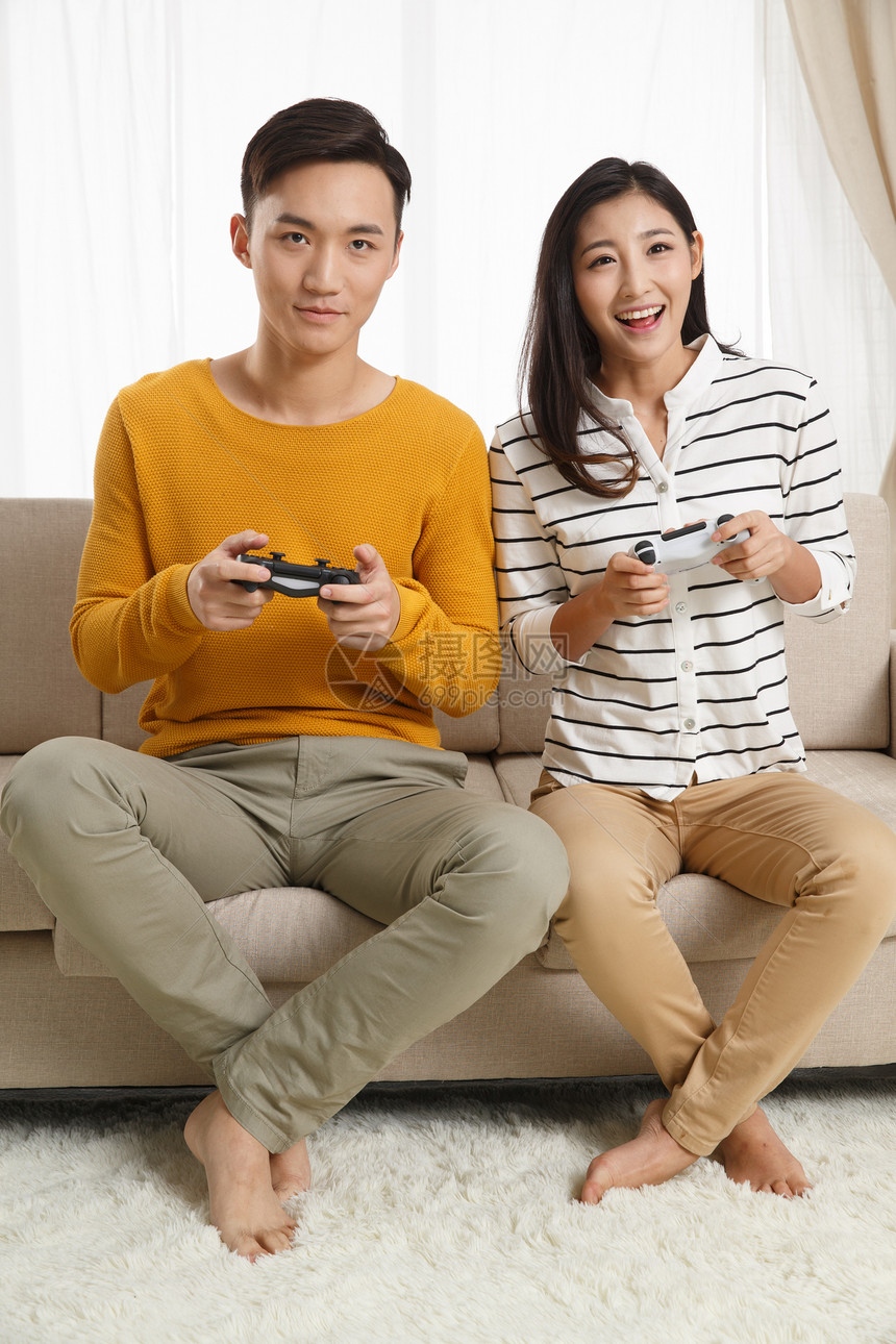 欢乐东亚20多岁青年情侣坐着沙发上玩游戏图片